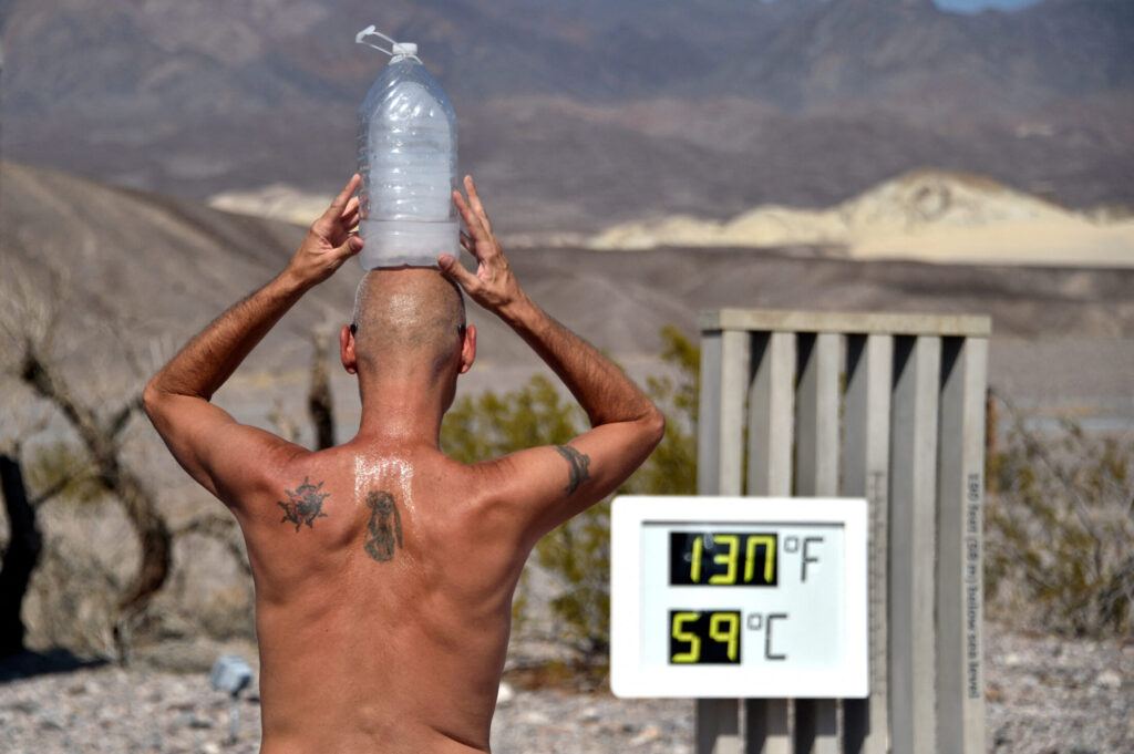 FILE PHOTO: Steve Krofchik of Las Vegas keeps cool with a bottle of ice on his head as the unofficial thermometer reads 130 degrees Fahrenheit (54.4 Celsius), with a mechanical fault on the display causing the numbers to render incorrectly, at the Furnace Creek Visitors Center in Death Valley, California, U.S. August 17, 2020. REUTERS/David Becker/File Photo