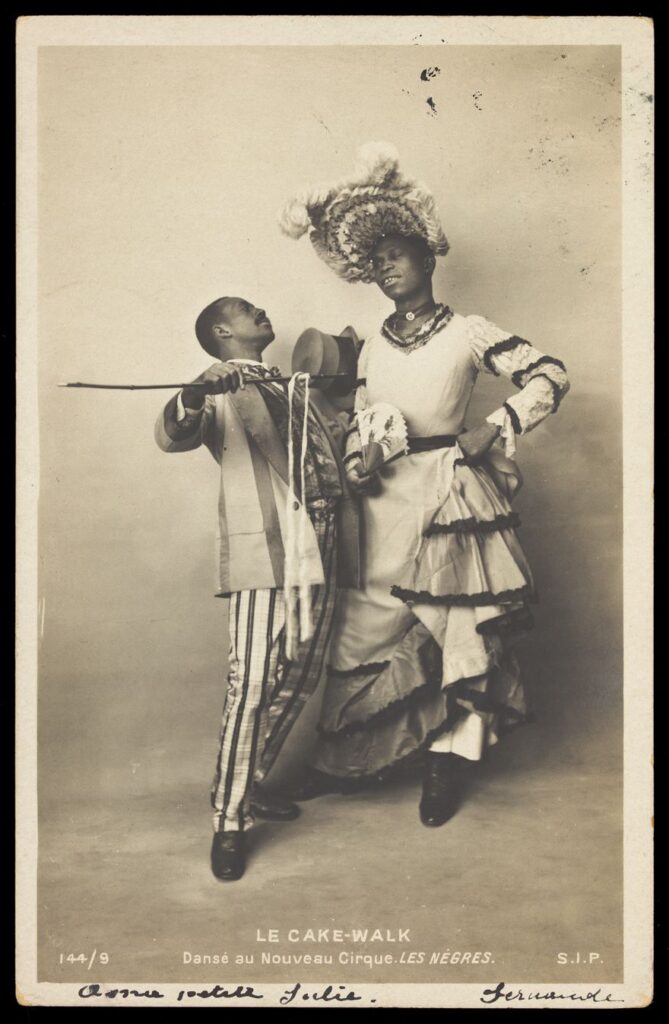 Two black actors, Gregory and Brown, one in drag, dancing the Cake-Walk in Paris. Photographic postcard, 1903