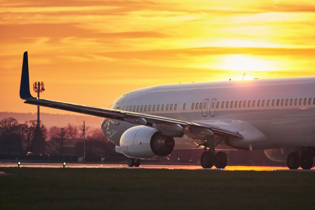 Airplane before take off on runway. Traffic at airport against sky during colorful sunset.