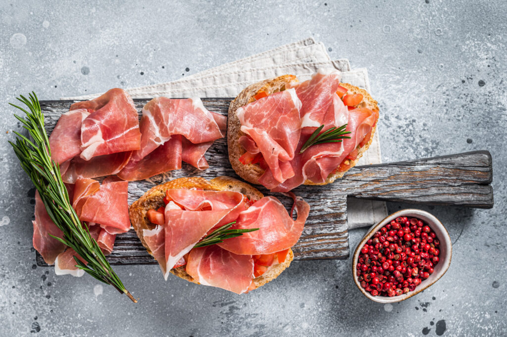 Spanish Tapas - Toast with tomatoes and cured Slices of jamon iberico ham on wooden board