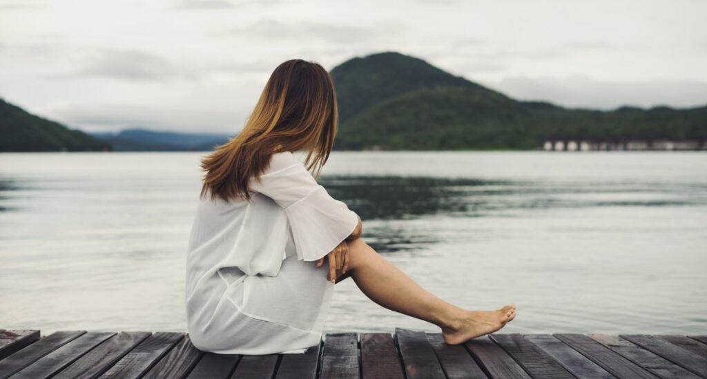 Γυναίκα βιώνει τα συναισθήματα της λύπης και της μοναξιάς κοντά σε λίμνη