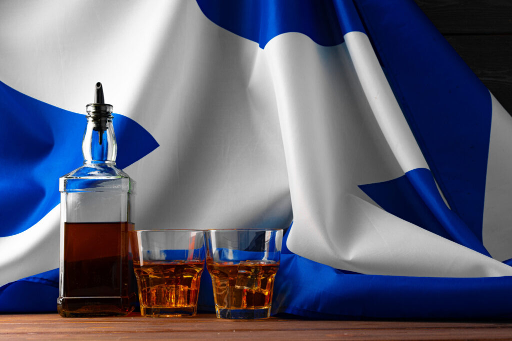 Ένα μπουκάλι ουίσκι και δύο ποτήρια μπροστά από την σημαία της Σκωτίας